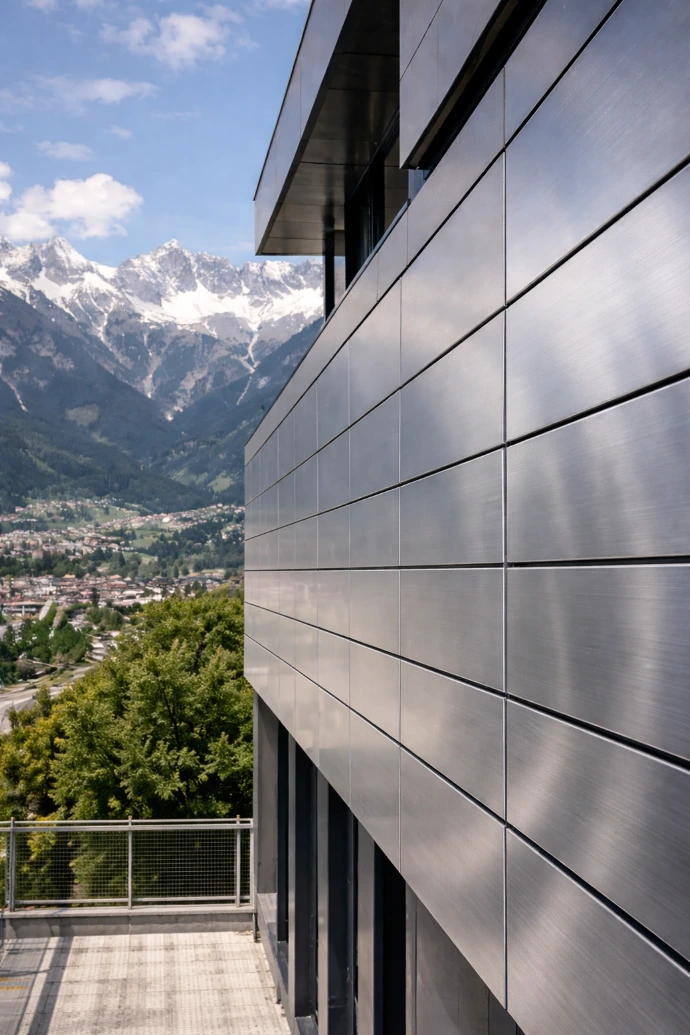 Moderne Edelstahl-Metallfassade eines Gebäudes in Innsbruck mit präziser Panelverkleidung und alpiner Bergkulisse im Hintergrund